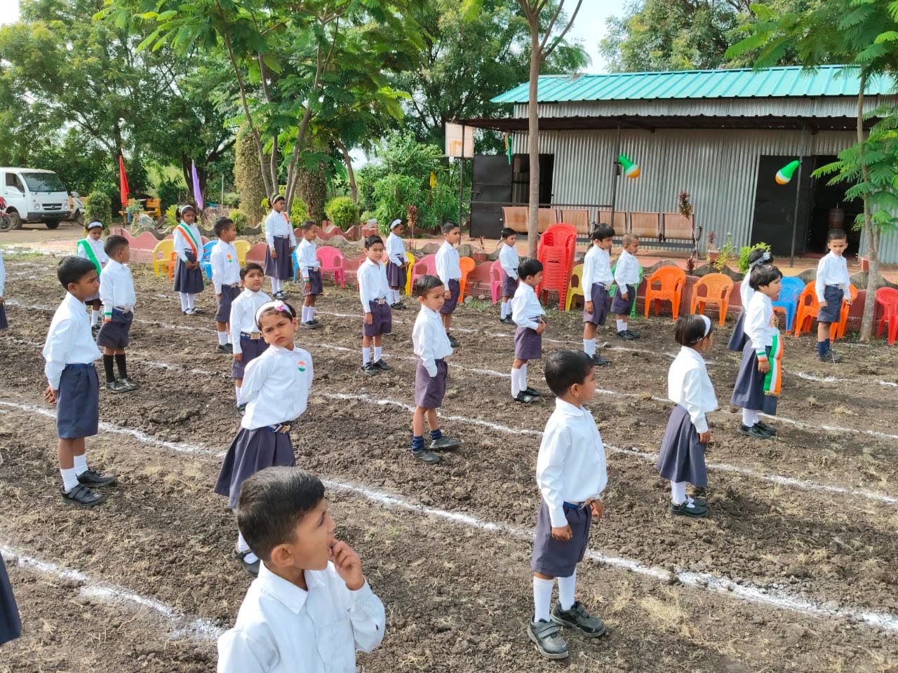 Children in white uniforms standing in straight lines marked with chalk on the school ground