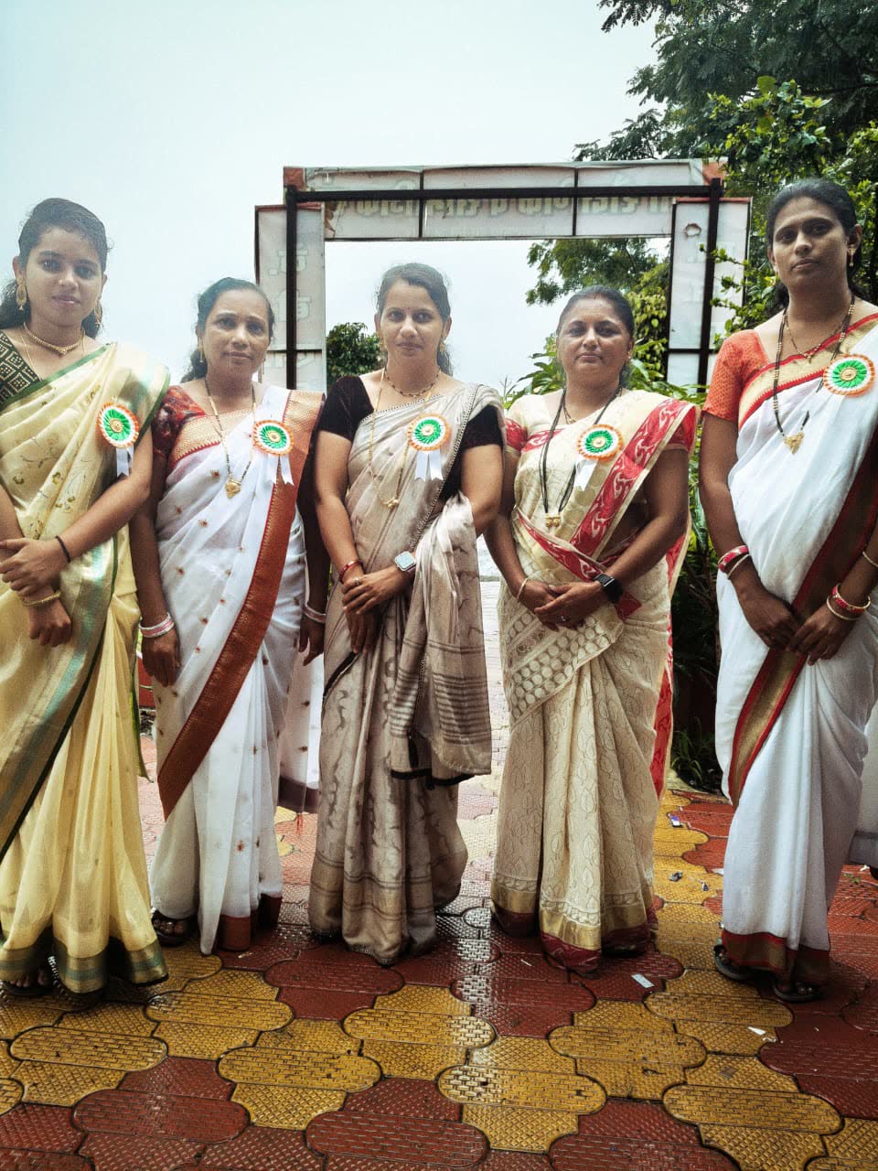 Five teachers in sarees with tricolour rosettes at the school gate